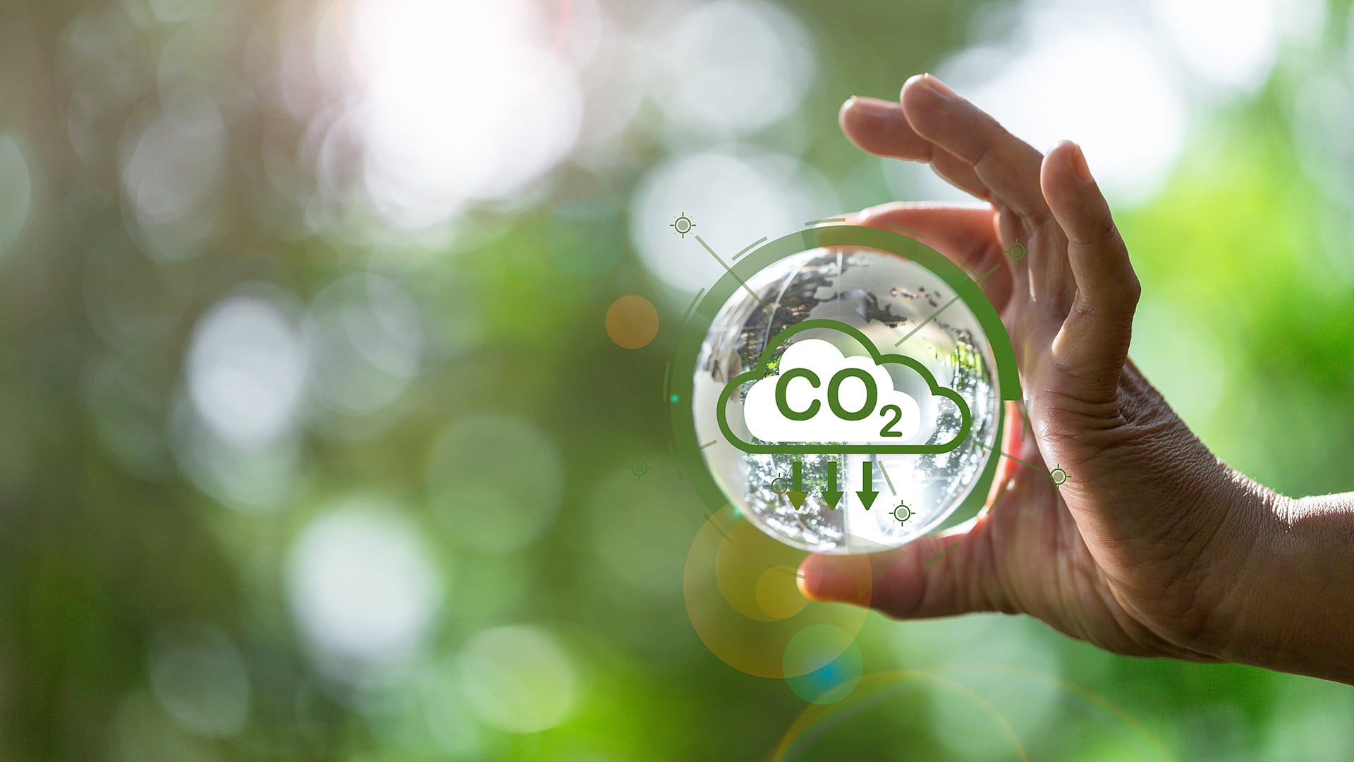 Ruka držiaca sklenenú guľu so symbolom CO₂ a šípkami nadol, znázorňujúca nízkoemisnú elektrinu pre firmy.
